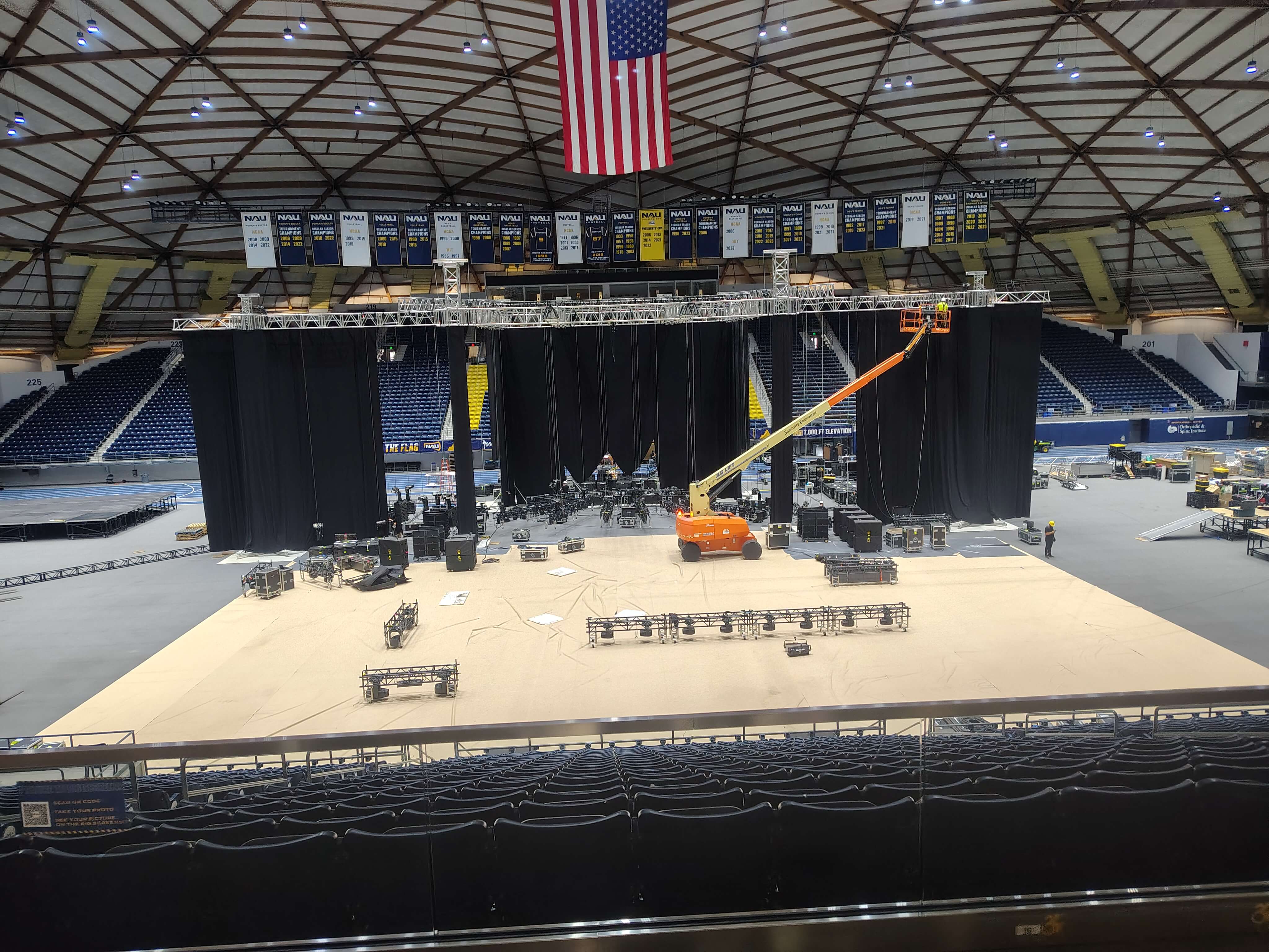 Arena load-in at NAU Skydome with a boom lift on stage and championship banners overhead
