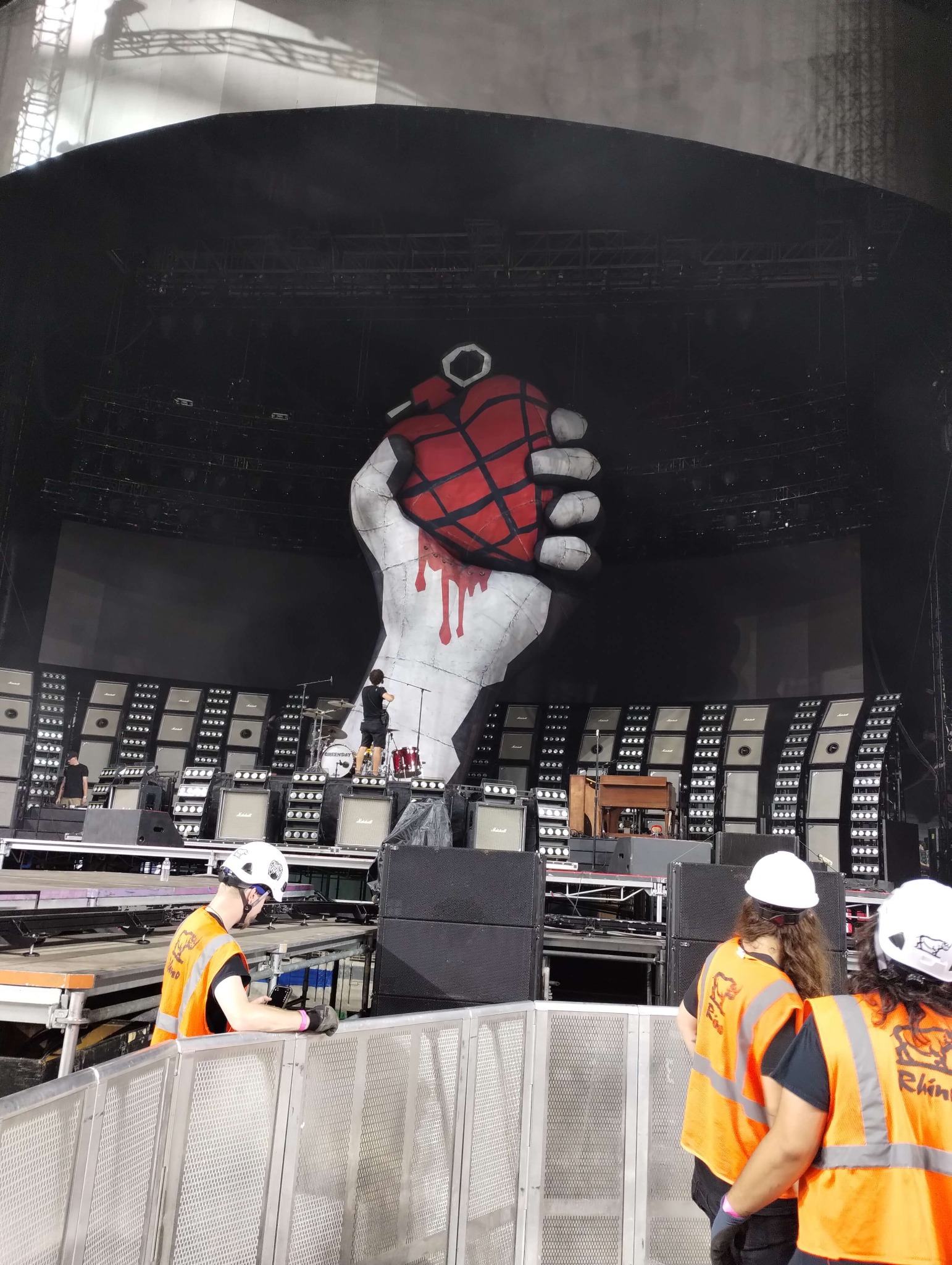 Stagehand crew installing crowd barricade in front of a large outdoor concert stage with Green Day backdrop art