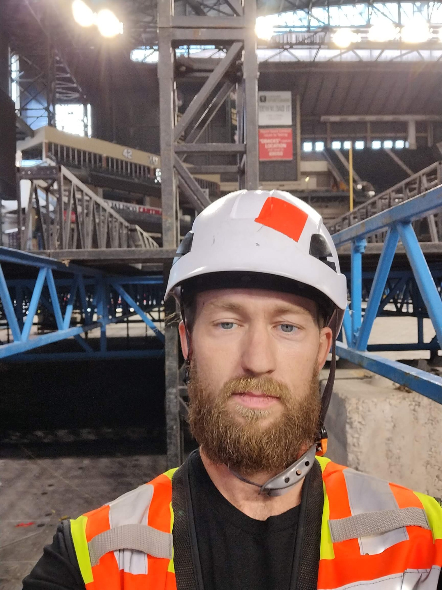 Aaron Bowman in hard hat and high-vis vest with large blue stage truss structure in background
