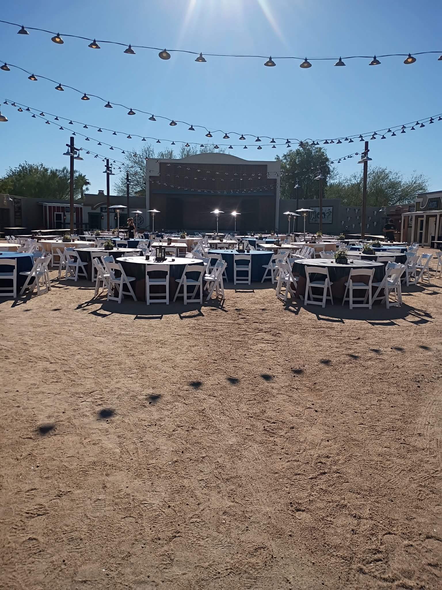 Outdoor event venue with round tables and string lights arranged facing a small stage