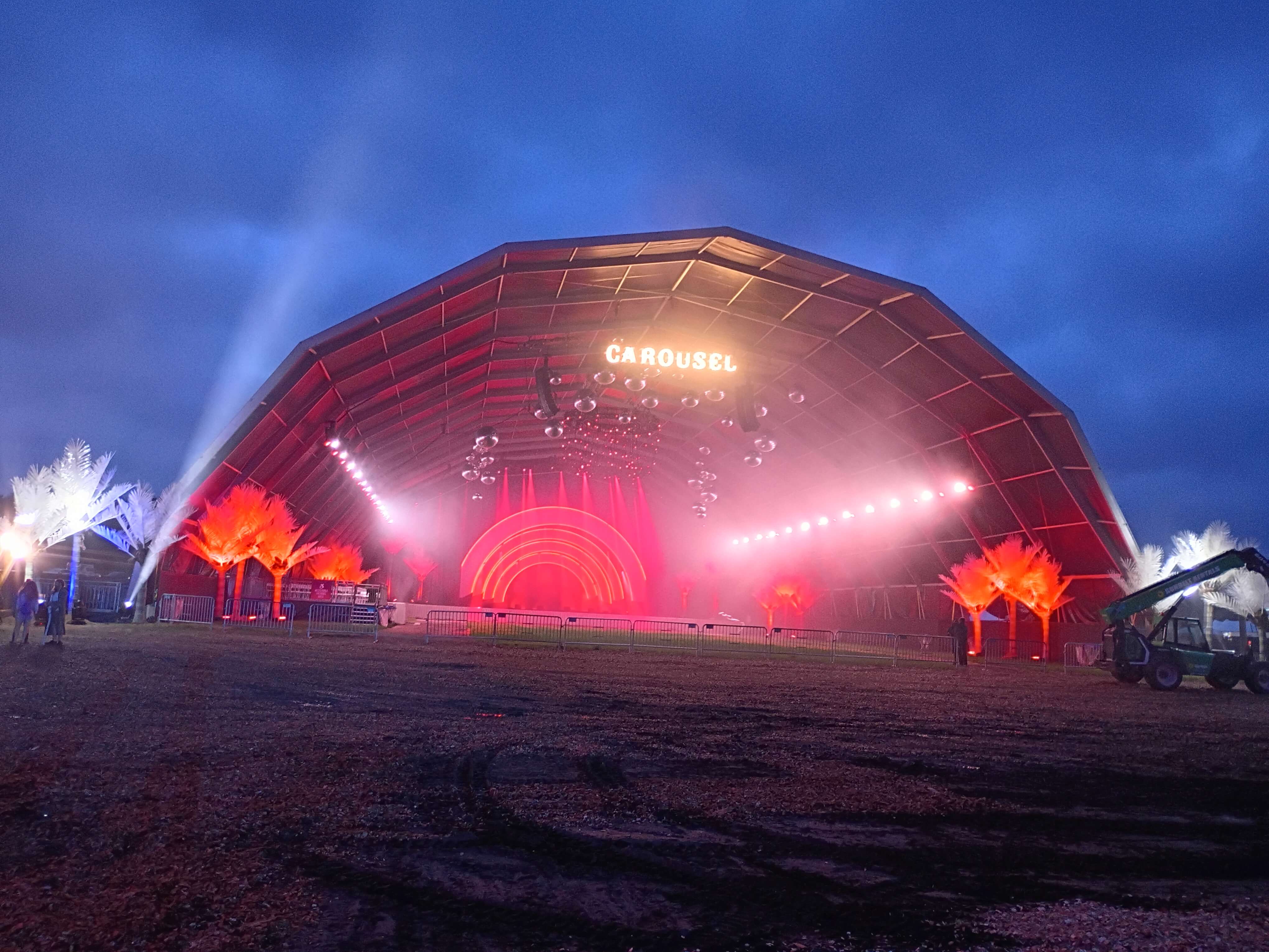 Carousel Club stage at Electric Forest 2025 lit in red with decorative illuminated palm trees and bubble art installations at dusk