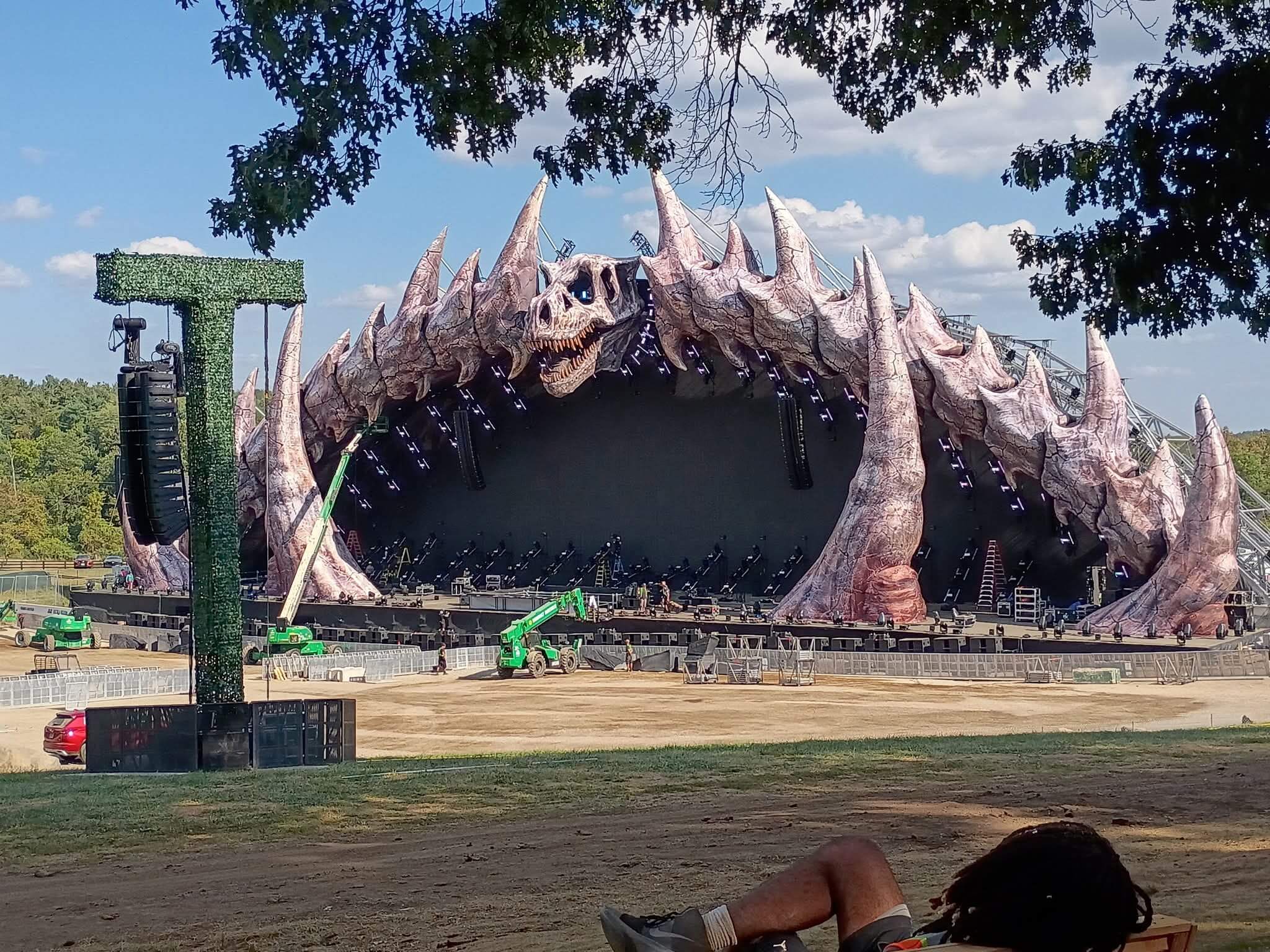Lost Lands festival main stage with massive monster skull scenic facade and production crew with lifts during load-in