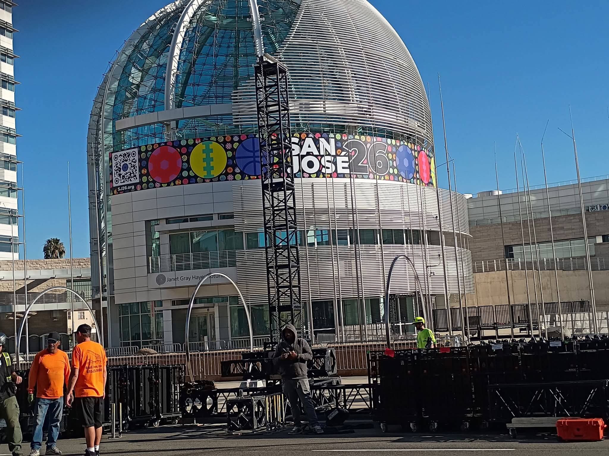 Super Bowl Host Committee event load-in with production crew and trusses in front of San Jose City Hall with SAN JOSE 26 branding